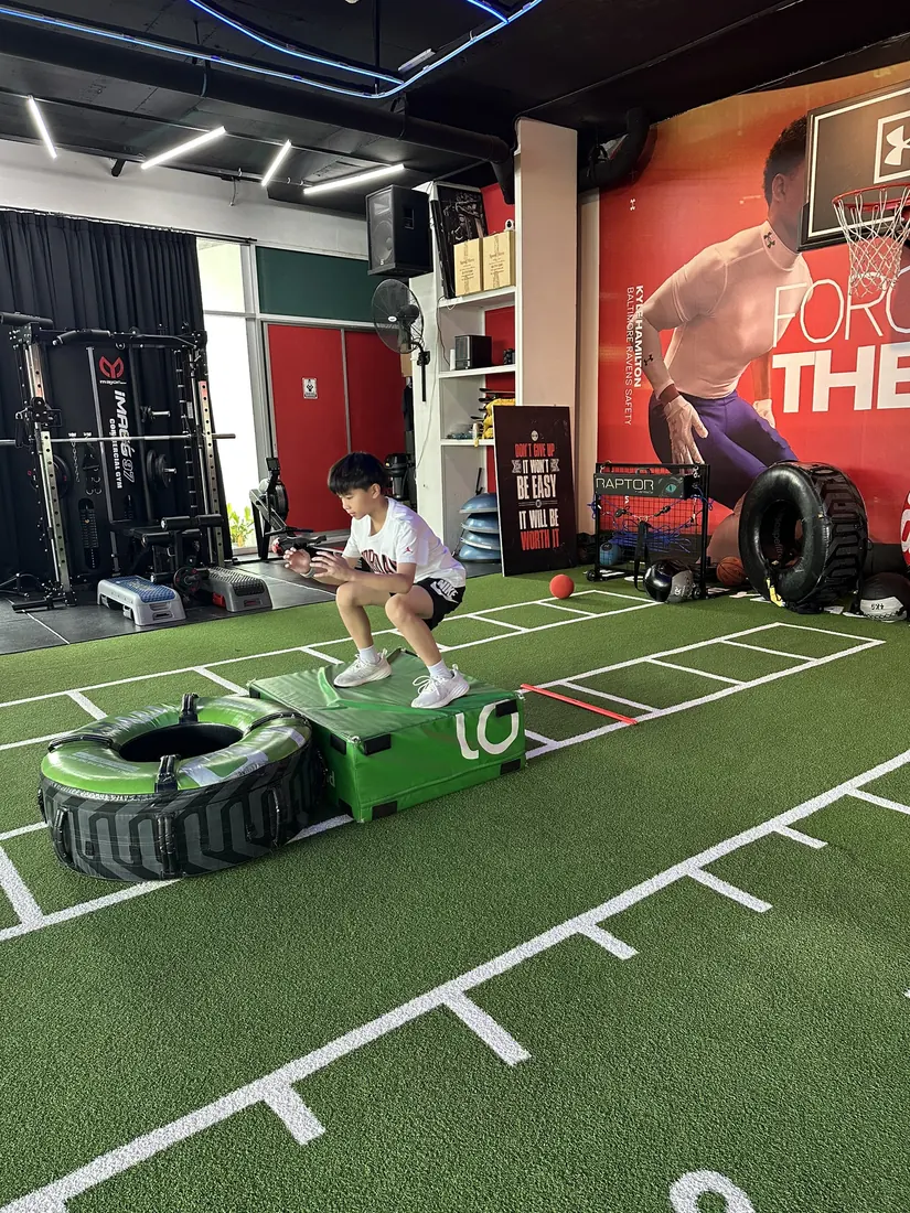 Young boy landing a box jump on the turf during Underdogs youth speed and power training, Bangkok