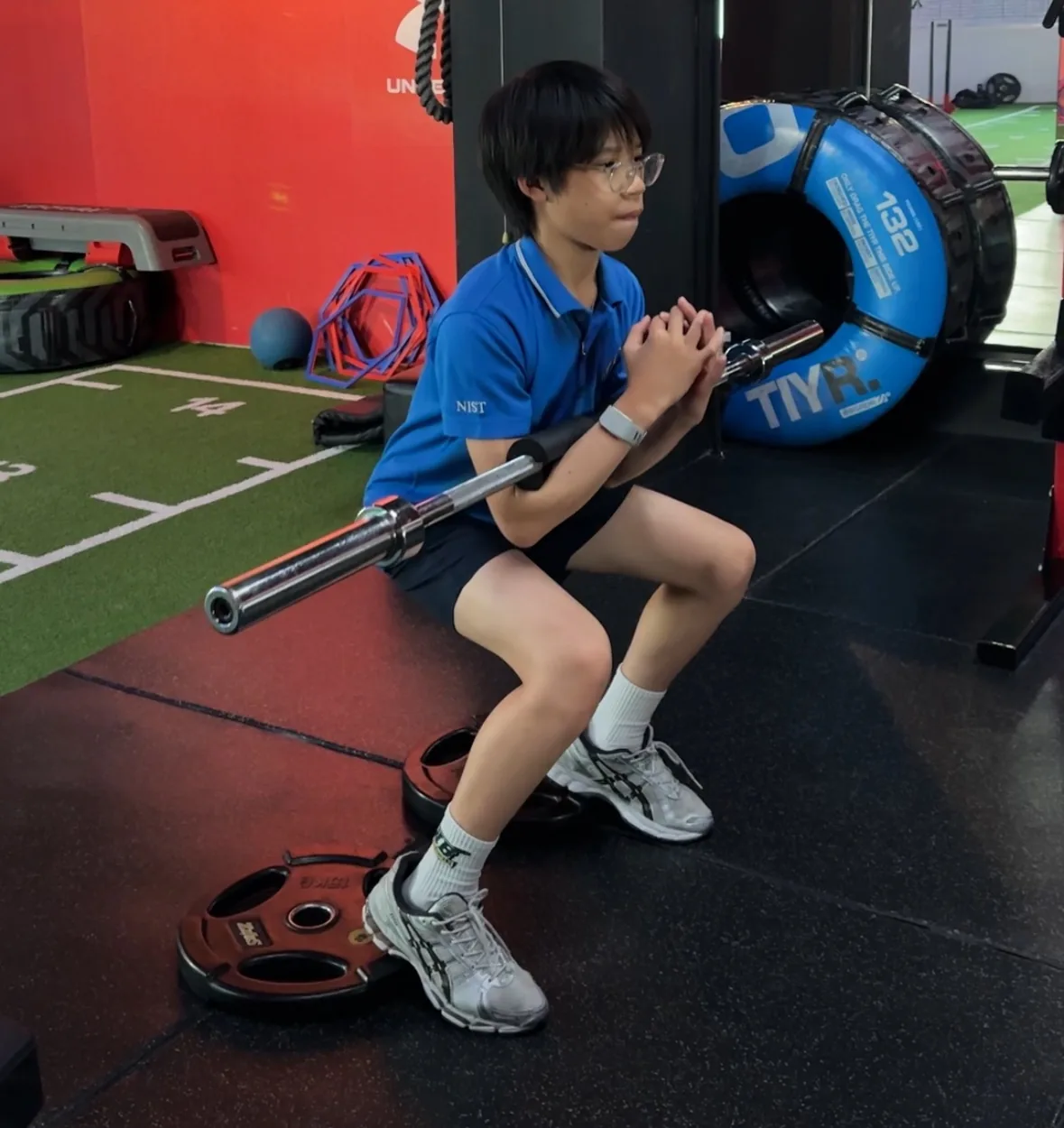 Teen learning squat technique with a barbell during youth strength training at Body By Beast, Bangkok