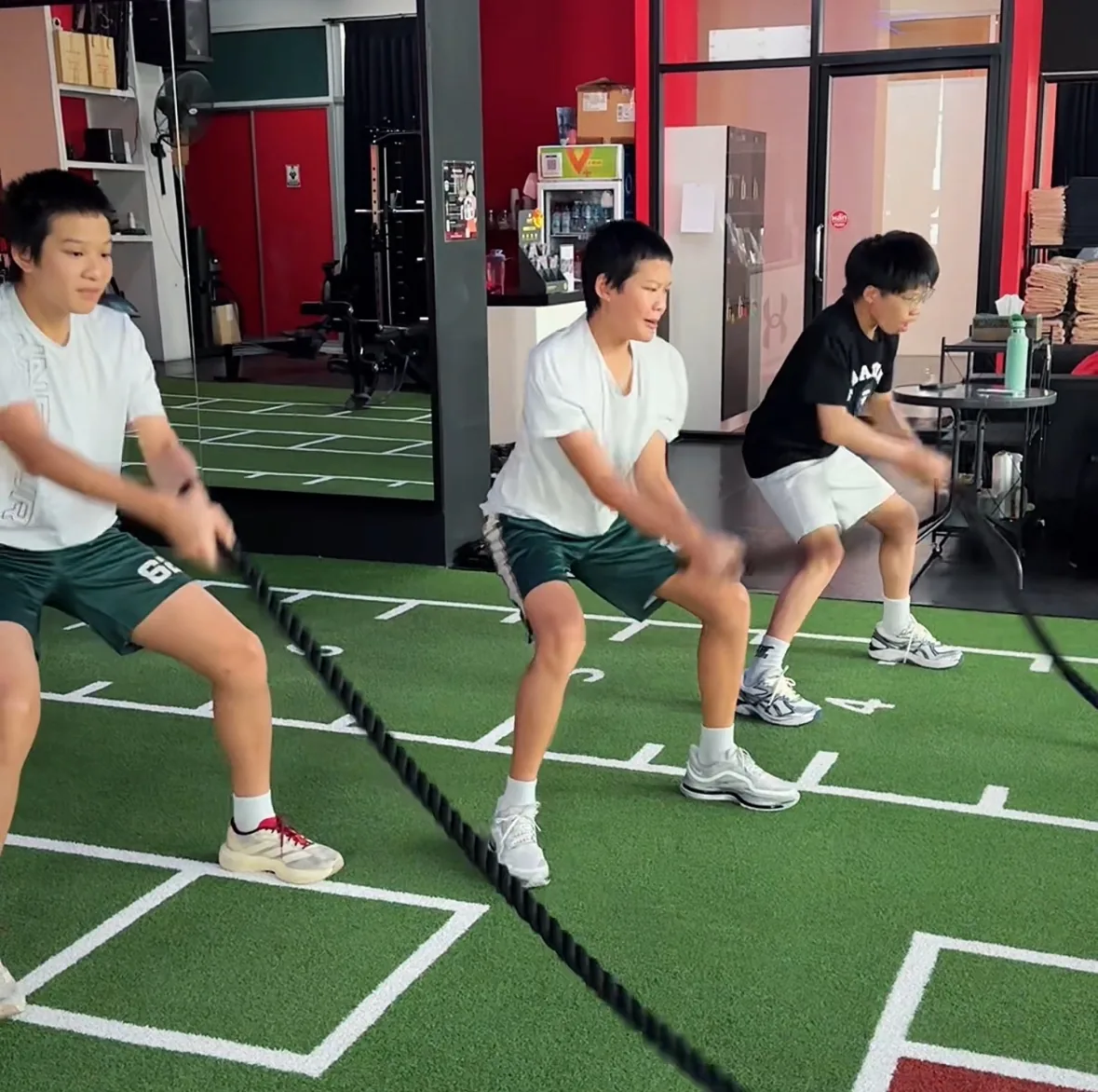 Three teenagers doing battle rope conditioning on the turf at Body By Beast, Bangkok