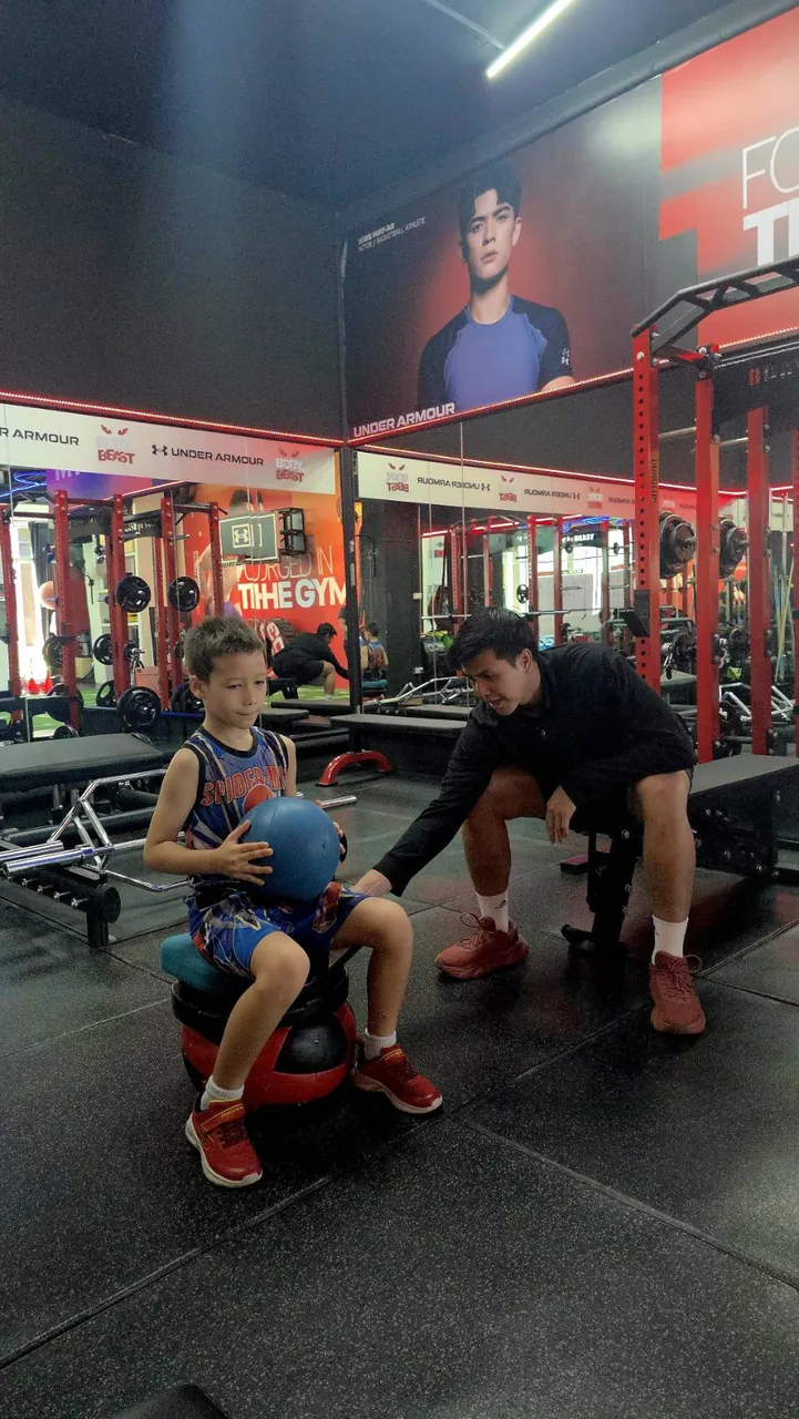 Coach guiding a young boy through a medicine ball balance drill at Body By Beast, Bangkok
