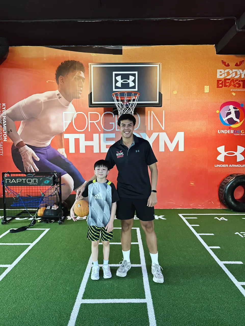 Young basketball player holding a ball with his Body By Beast coach in the Underdogs kids training area, Bangkok